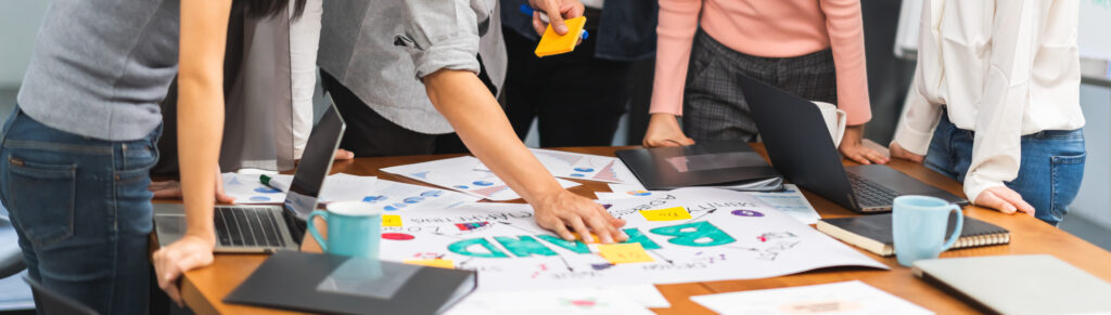 een groep werkt samen tijdens een brainstorm sessie, waar ze alle rond documenten op een tafel staan